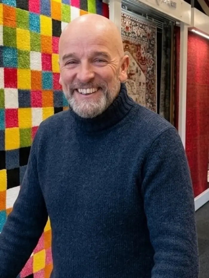 Pascal, fondateur du Roi du Tapis, souriant devant le mur de tapis du showroom