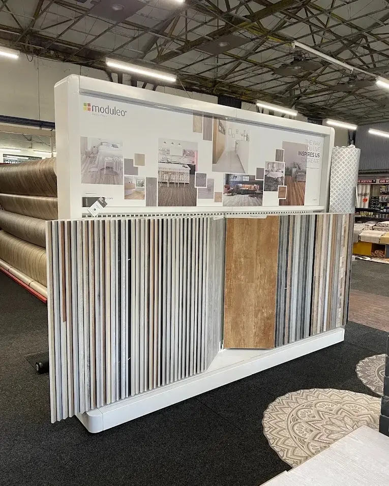 Intérieur du showroom : présentoir de lames de sol, rouleaux et tapis sous la charpente