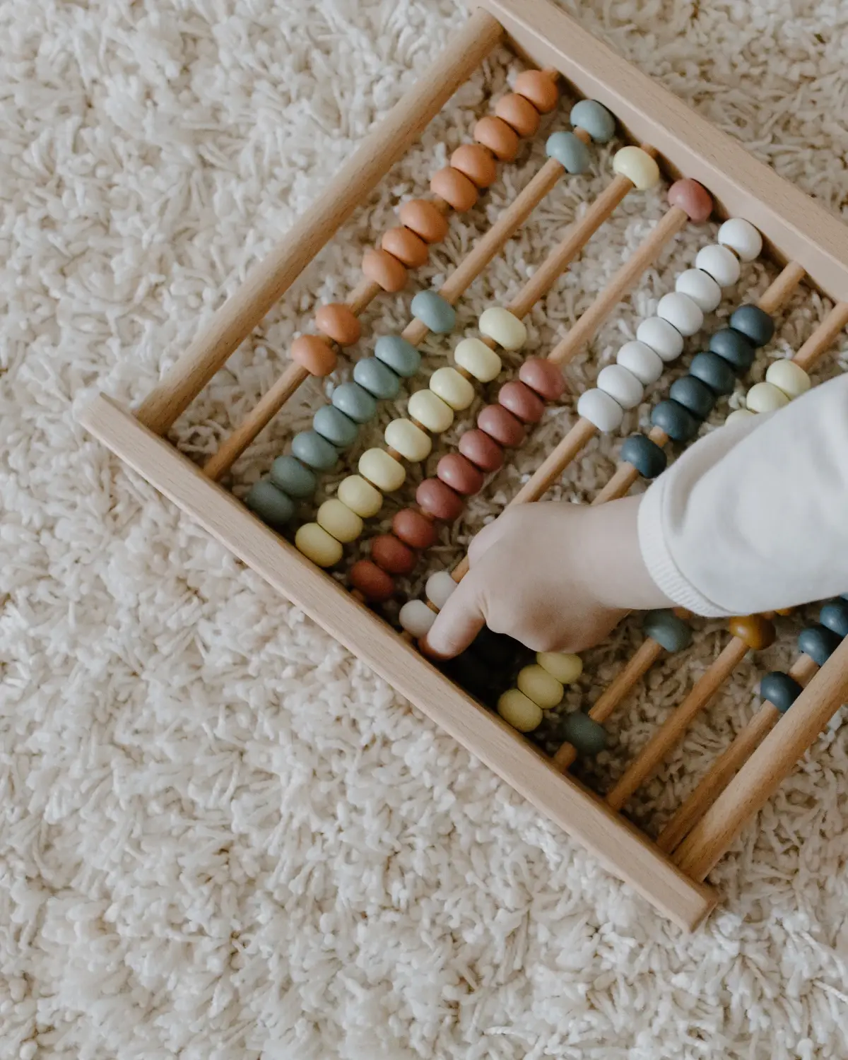 Enfant qui joue avec un boulier en bois sur un tapis épais